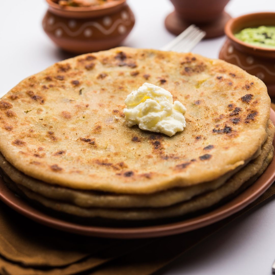 Aloo Paratha or Indian Potato stuffed Flatbread with butter on top. Served with fresh sweet Lassi, chutney and pickle . selective focus